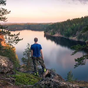 Kuvassa retkeilijä katsoo suomalaista järvimaisemaa korkealta kalliolta