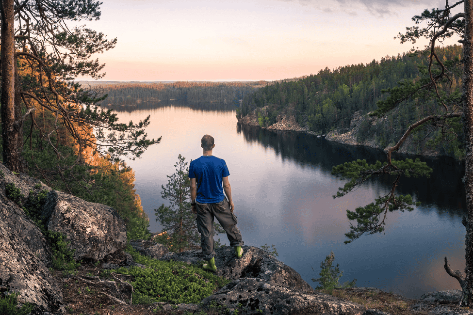 Kuvassa retkeilijä katsoo suomalaista järvimaisemaa korkealta kalliolta.